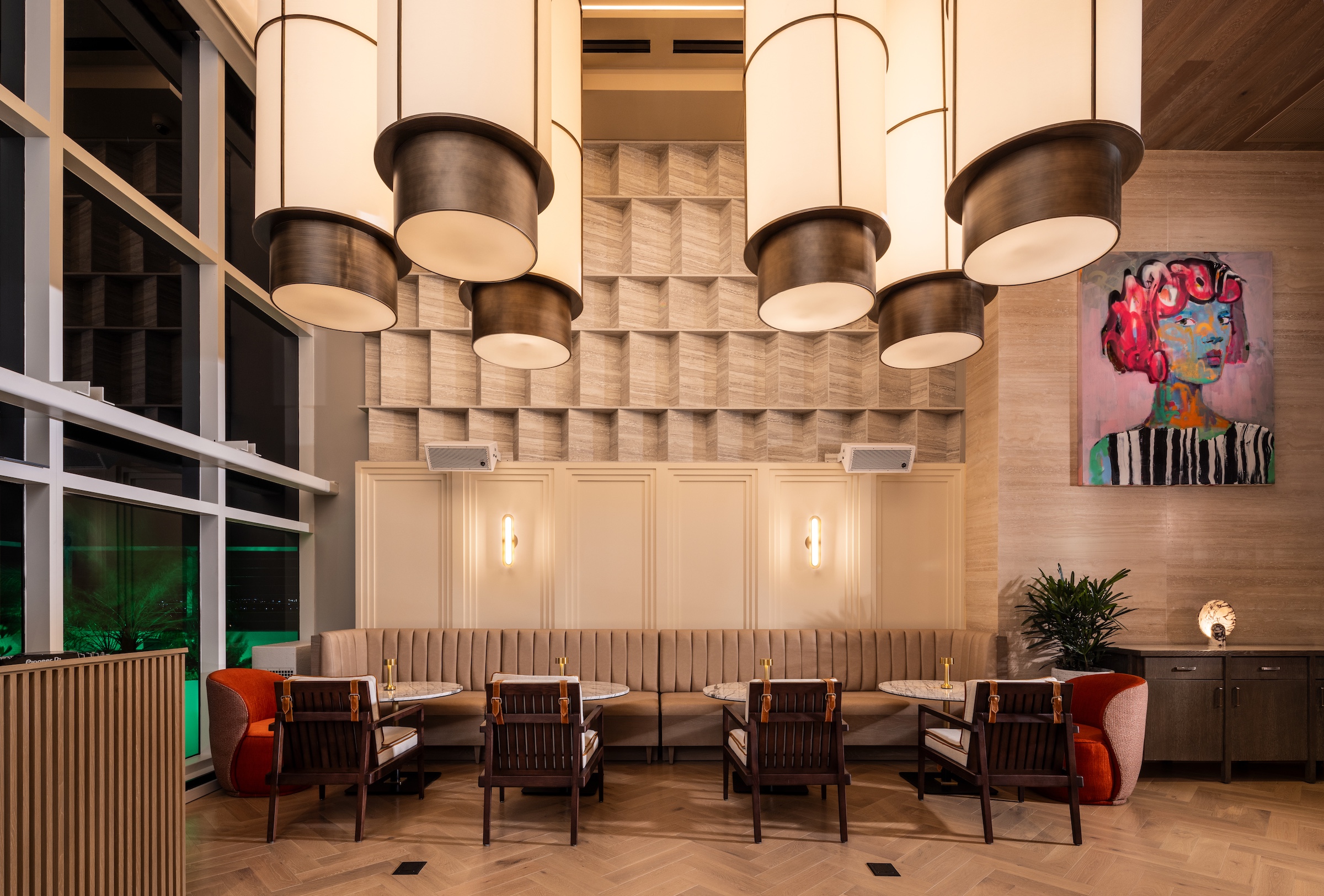 A restaurant bar decorated with large pendant lights, a textured wall, and a modern multi-colored painting of a woman
