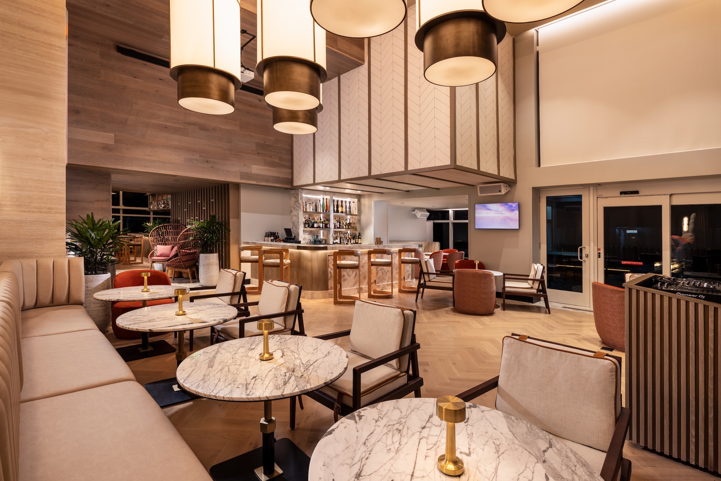 A trendy modern dining area with a long padded bench and marble two-top tables, next to a corner bar