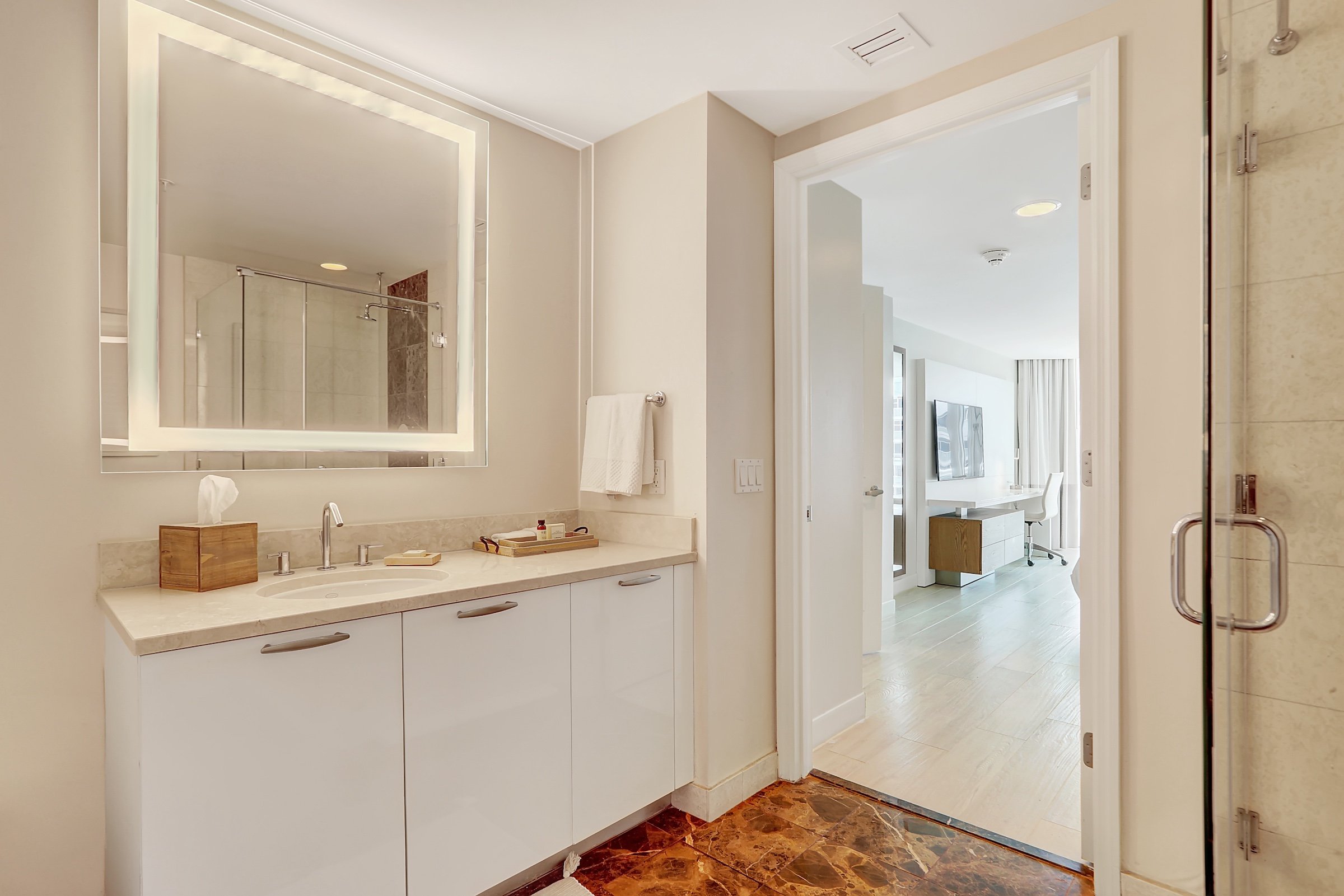 A bathroom with cream colored walls a marble sink and brown marbled floor