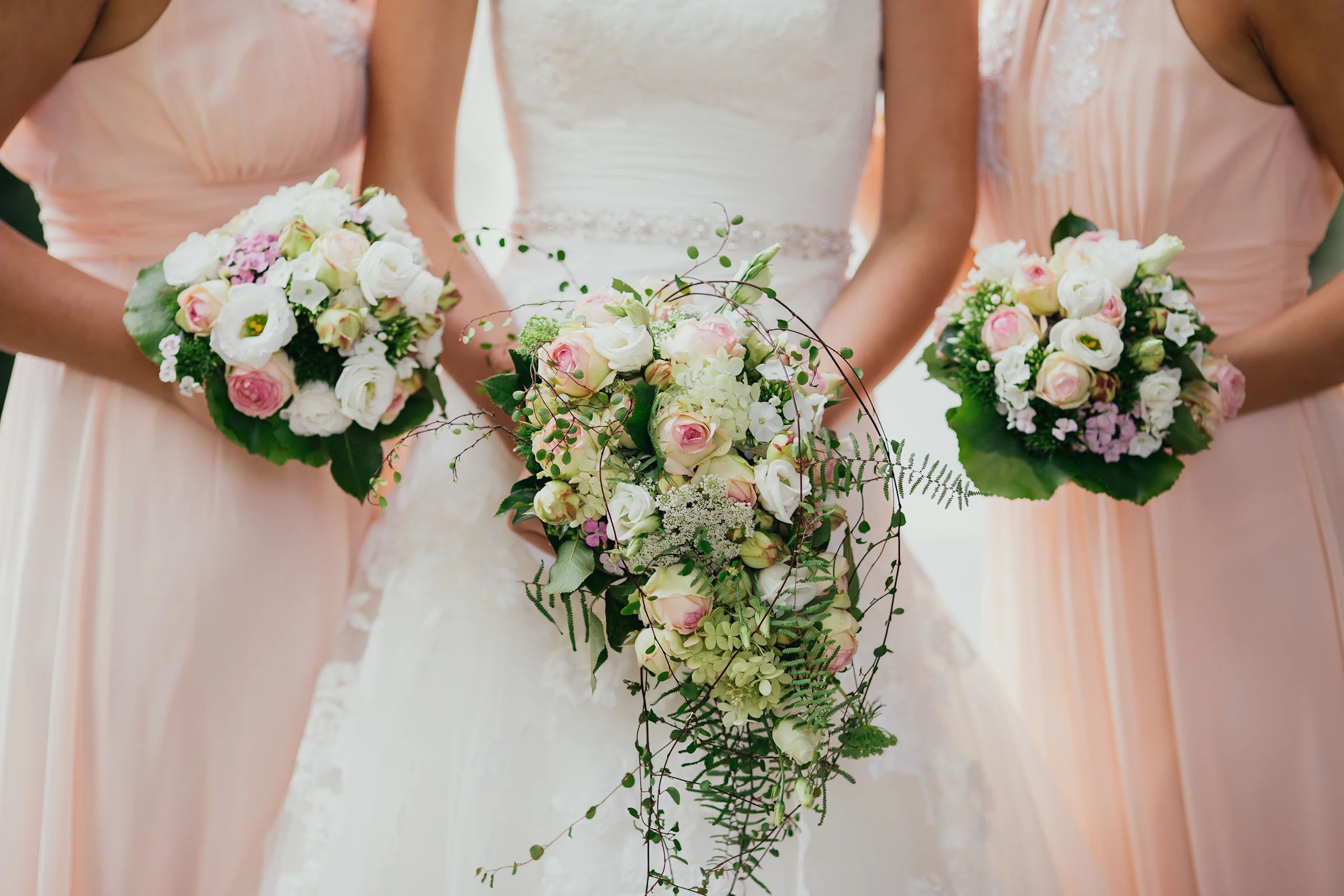 Three bridesmaids standing, holding bouquets of flowers