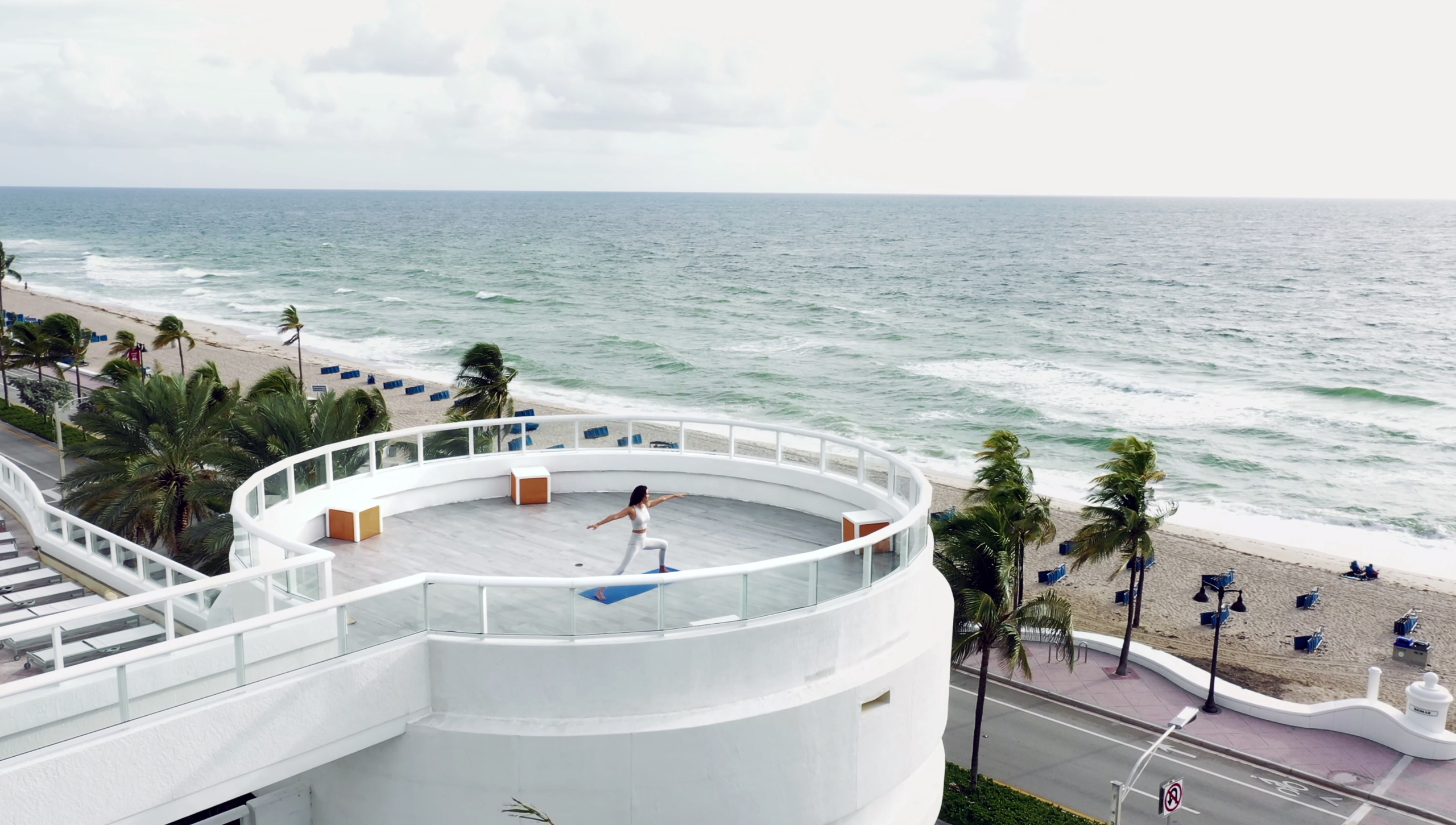 An aerial view of a person doing yoga on a large oceanside rotunda platform