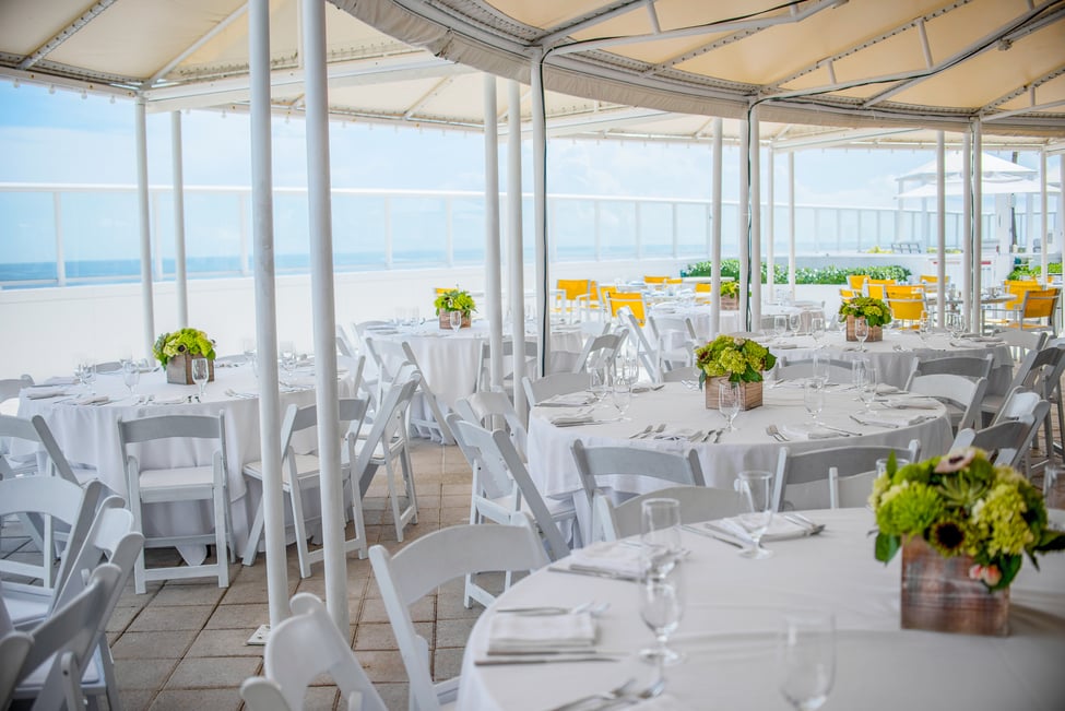 A beachfront terrace with round banquet tables topped with white linens