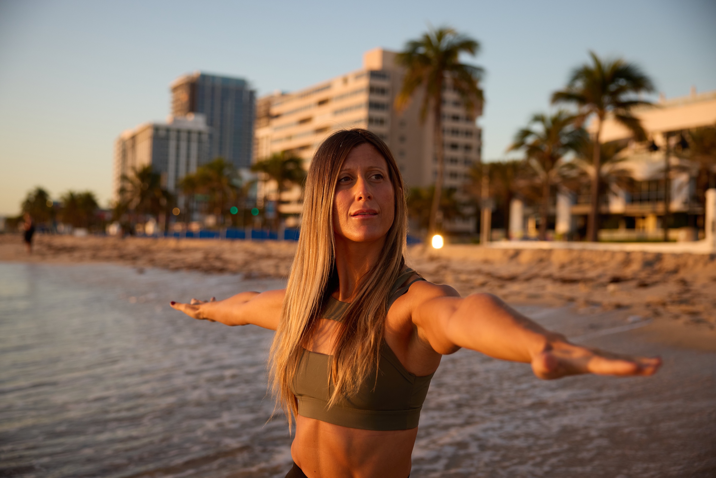 A woman performs warrior yoga pose near the ocean on Fort Lauderdale beach