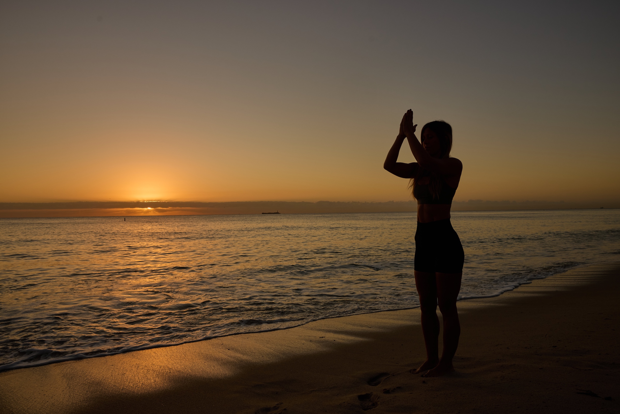 A woman in silhouette making a meditative pose on the beach at sunrise