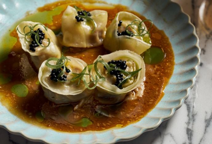 A stuffed pasta dish in a bowl of broth, topped with fresh greens