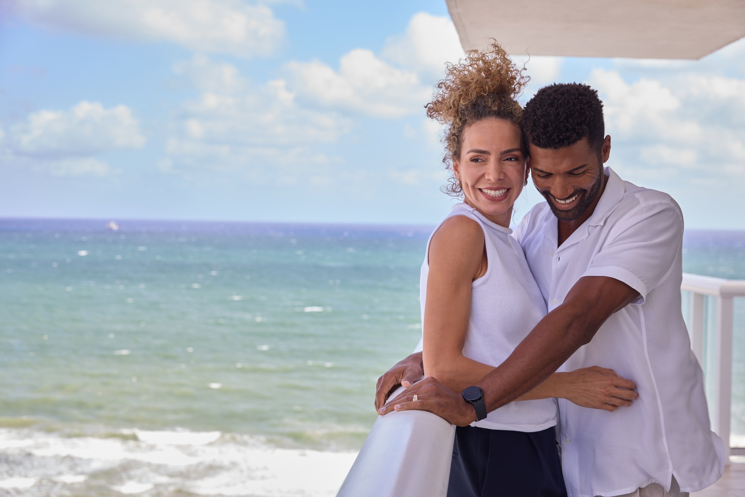 a couple stand close on a balcony with ocean in the background