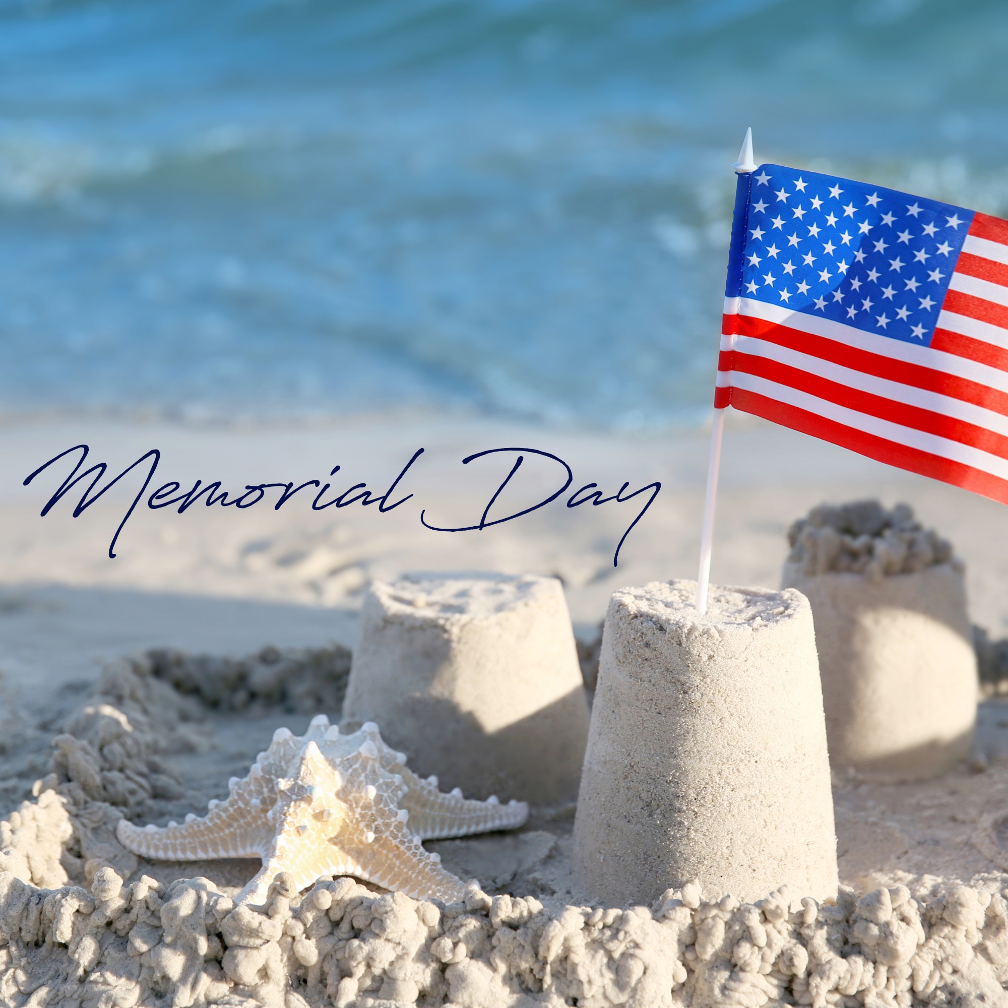 A miniature American flag sticking out of a sandcastle on the beach, with the words