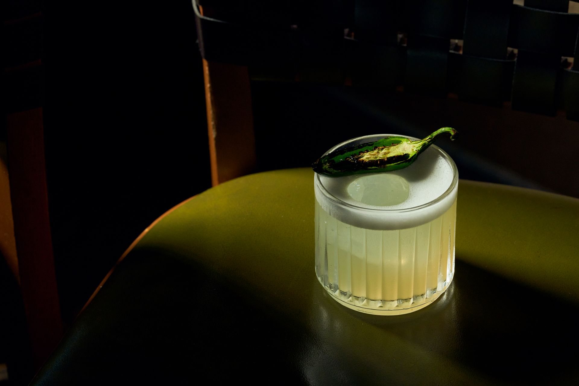 a lime green cocktail in a rock glass with a grilled jalapeño on as garnish