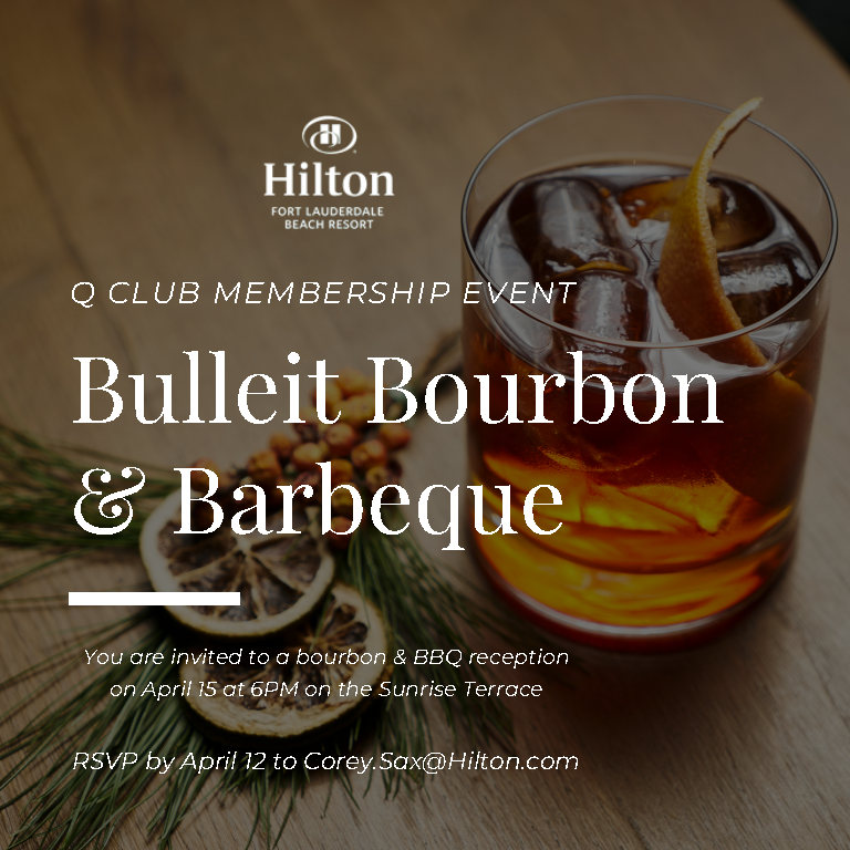a glass of bourbon on a wood table next to a sprig of green
