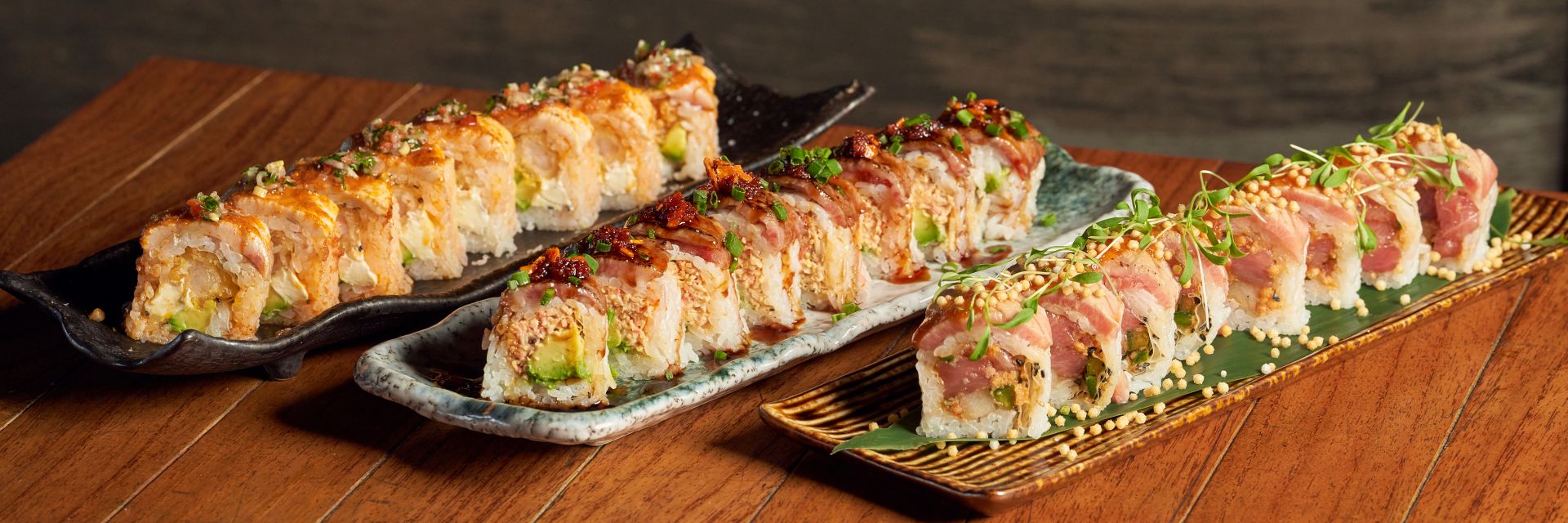 three plates of maki upon a wooden table