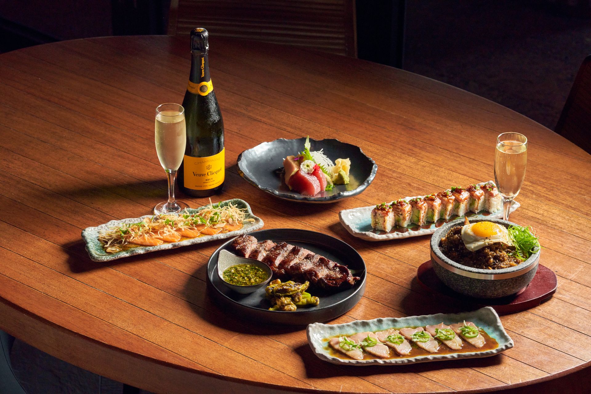 various asian inspired dishes along with a Champaign bottle and two flute glasses upon a wood table