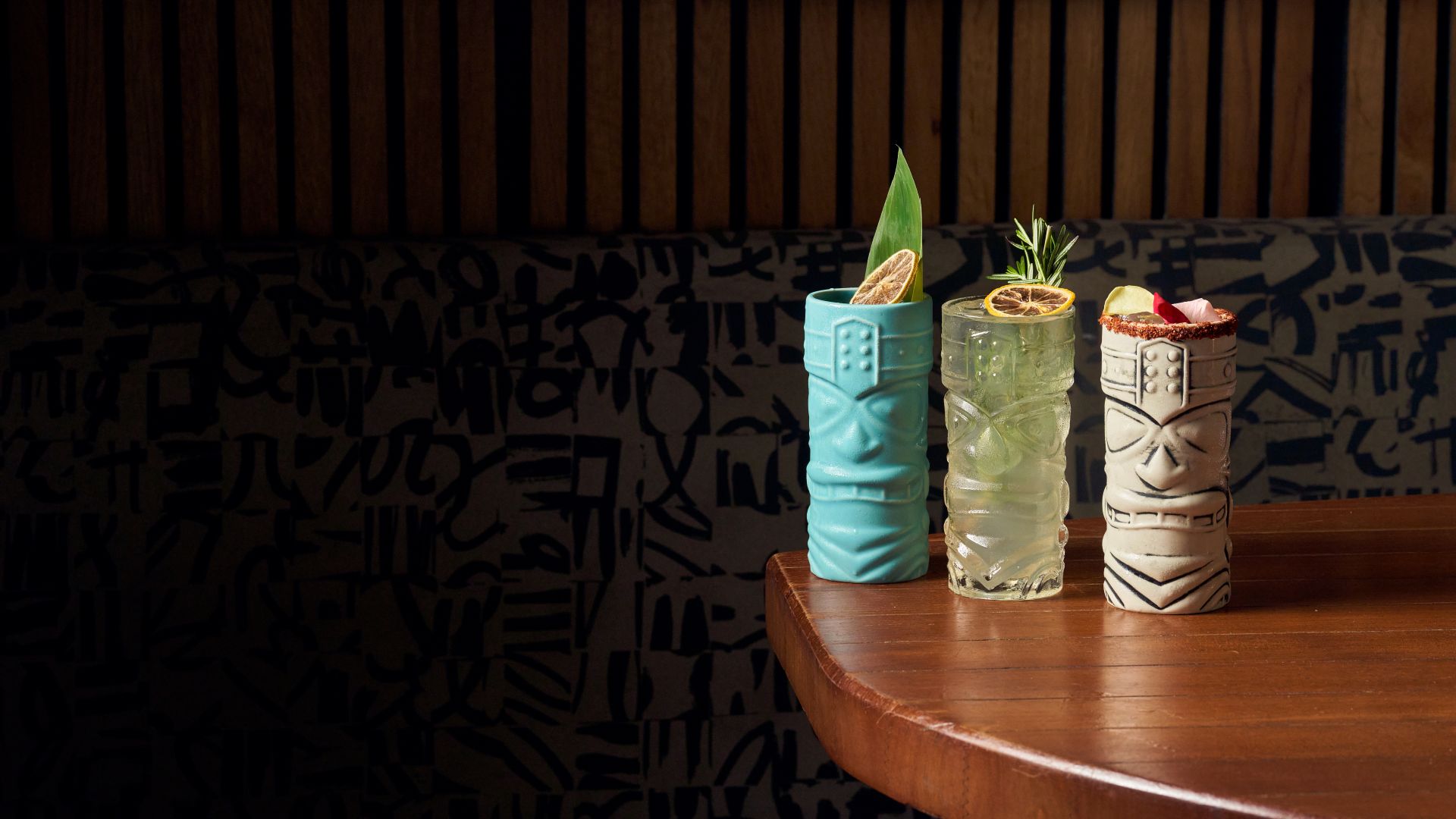 a blue, clear and stoneware tiki cocktail glasses upon a wood table