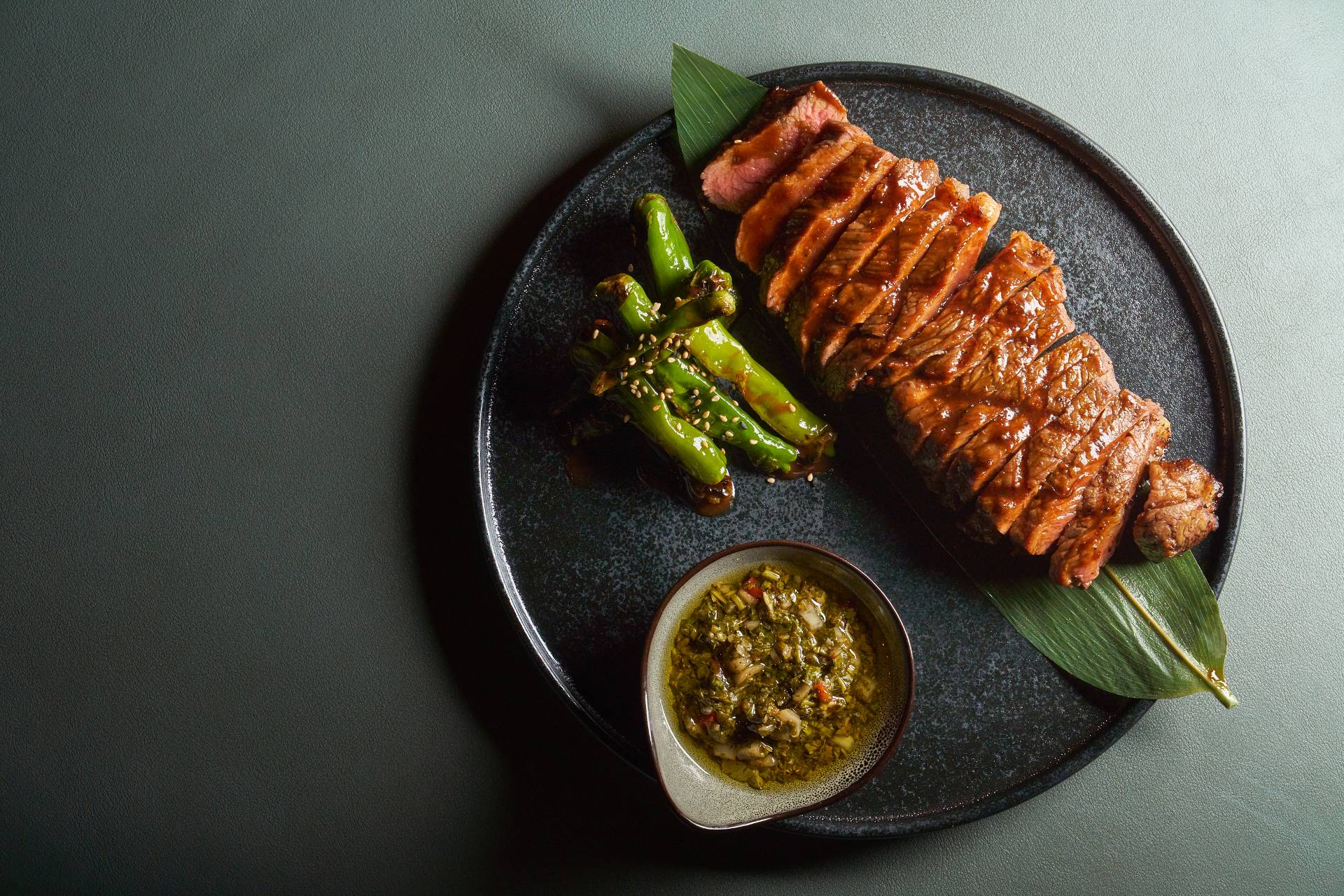 sliced steak on a black stoneware plate upon a forest green background